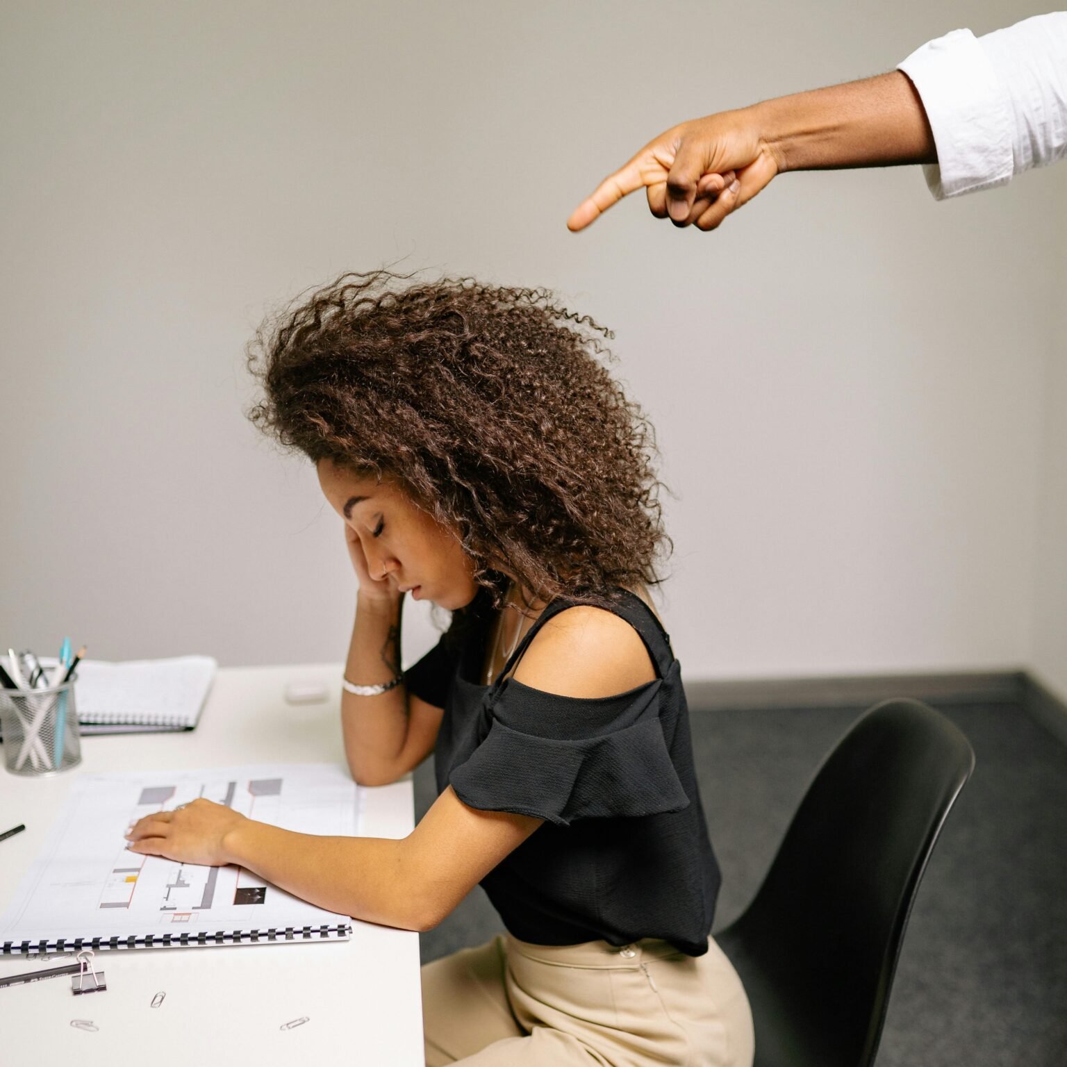 A stressed woman at her desk facing workplace tension from finger pointing.