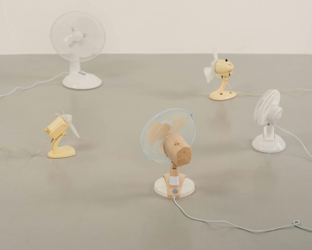 A variety of small desk fans positioned on a neutral floor showcasing design and color diversity.