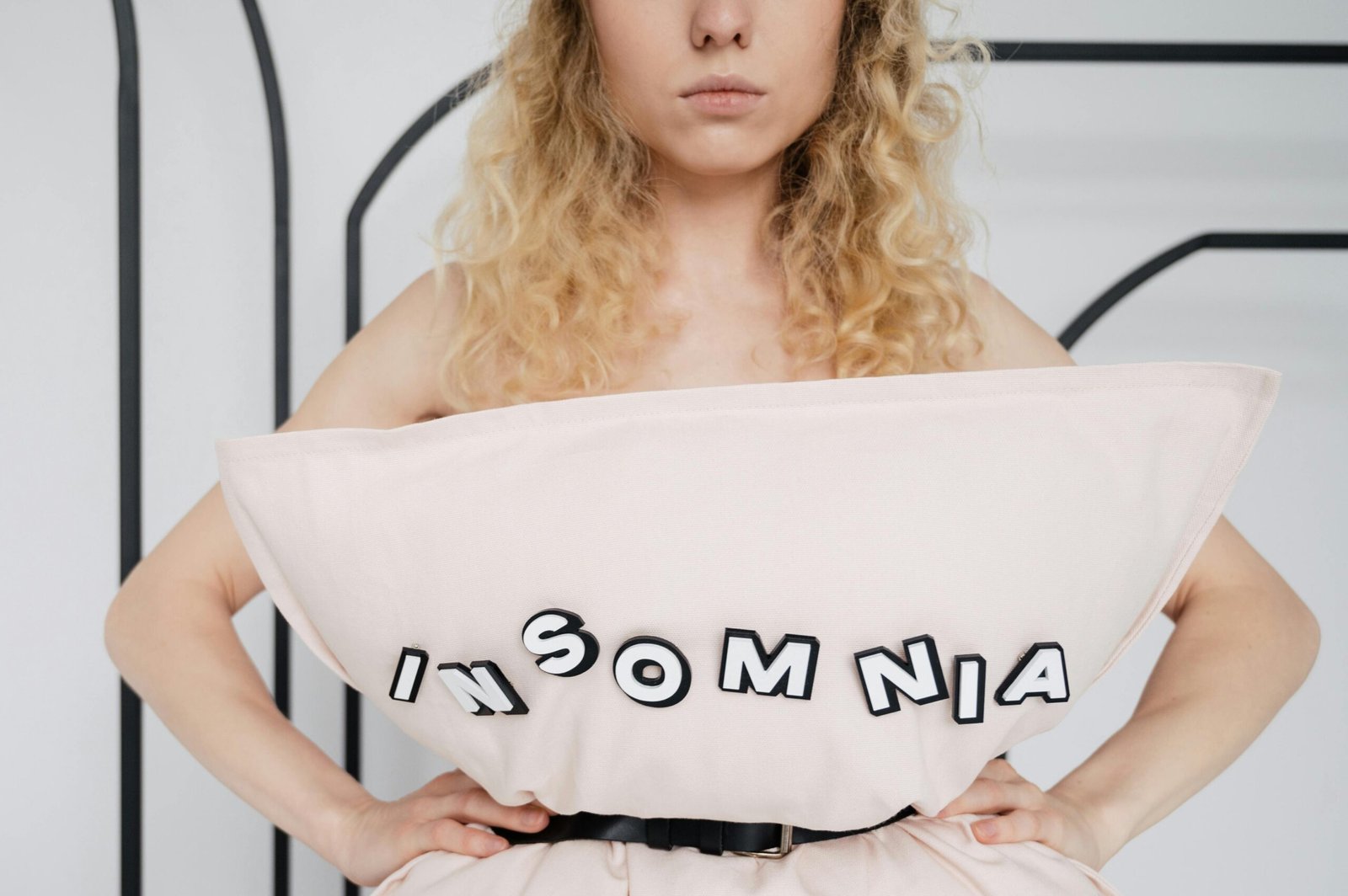 A woman poses with a pillow labeled 'insomnia' highlighting sleep disorders and mental health awareness.