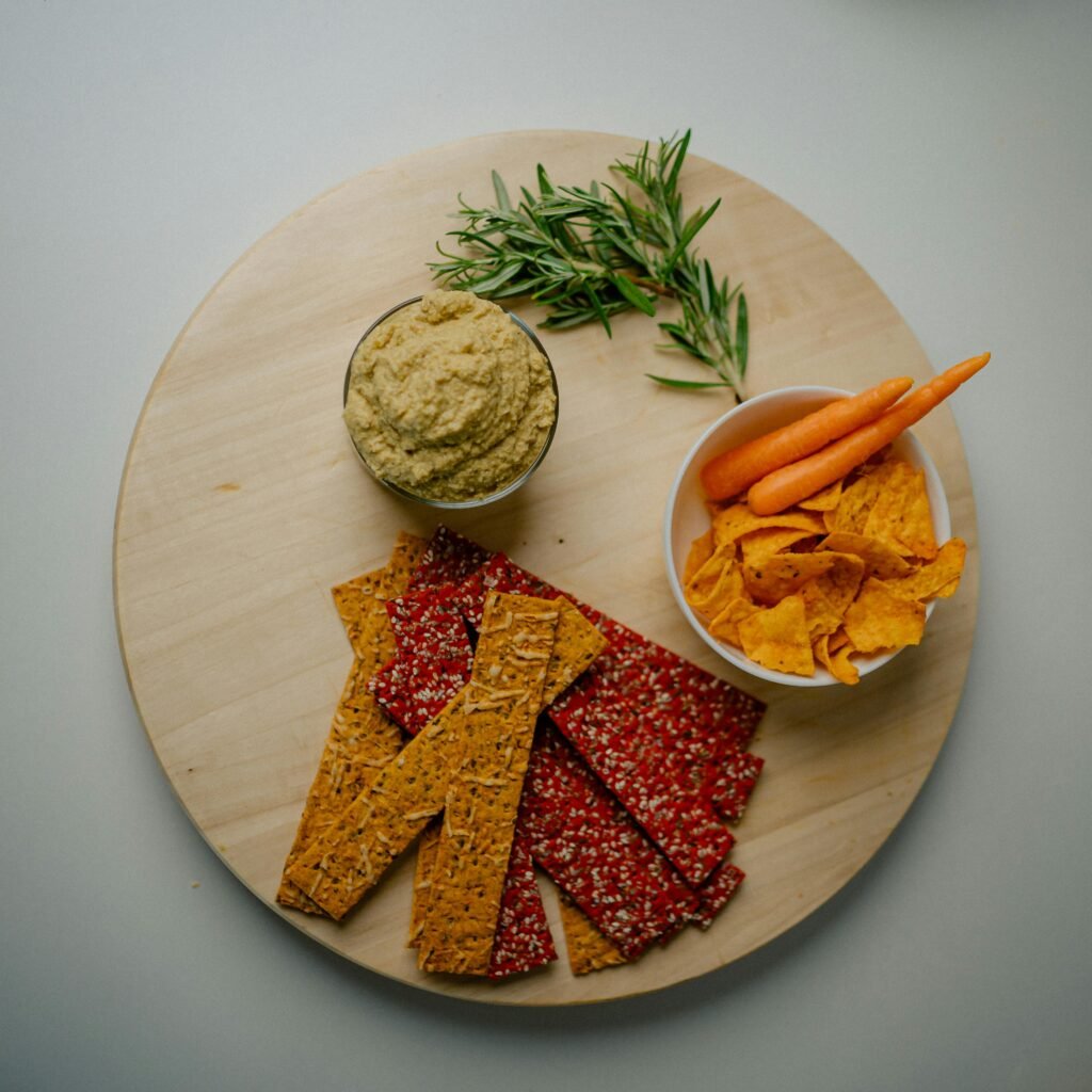 Top view of a nutritious snack platter featuring crackers, dip, and vegetables on a wooden tray.